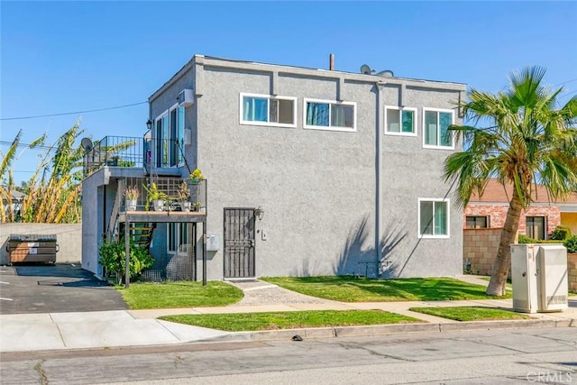 view of front of property featuring stairway, stucco siding, and a front lawn