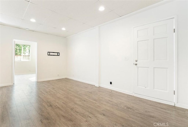 empty room featuring recessed lighting, a paneled ceiling, baseboards, and wood finished floors