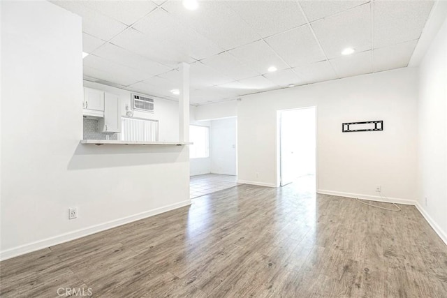 unfurnished living room featuring recessed lighting, a drop ceiling, baseboards, and wood finished floors