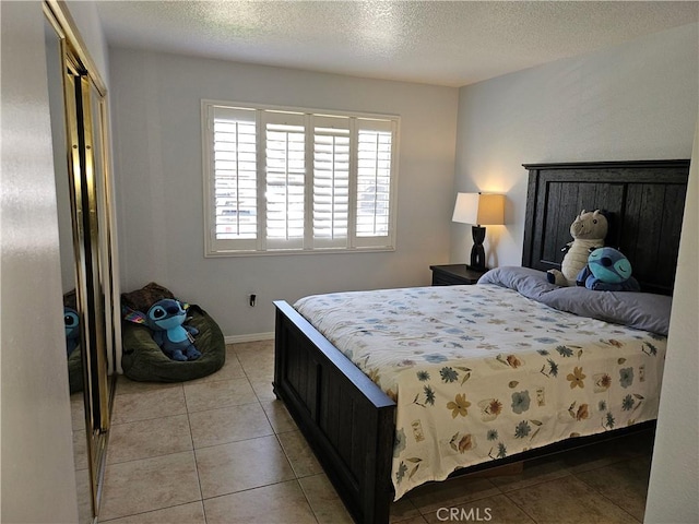 bedroom featuring light tile patterned flooring, baseboards, a textured ceiling, and a closet