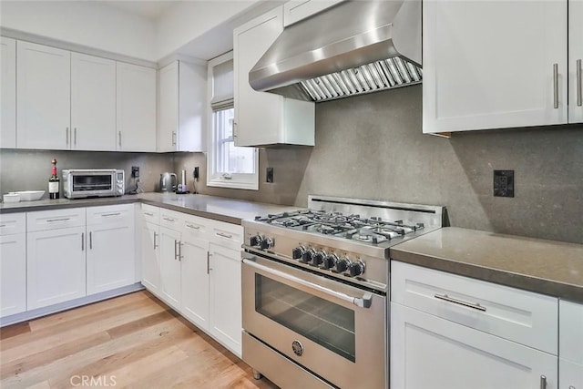 kitchen featuring high end stainless steel range, white cabinets, and wall chimney range hood