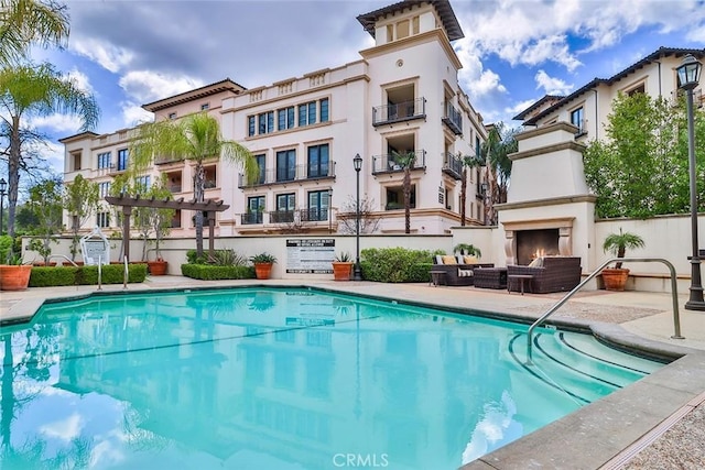 pool with an outdoor living space with a fireplace and a patio