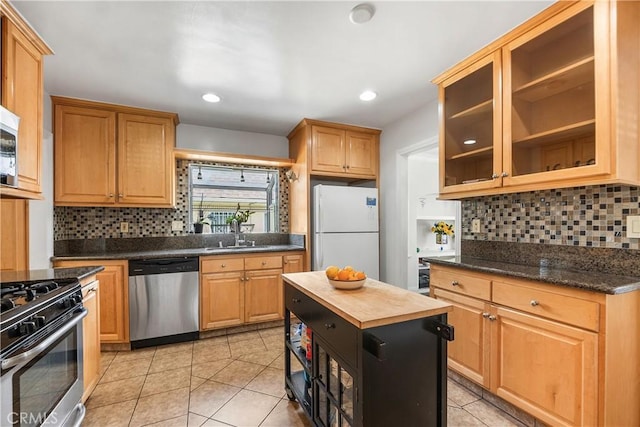kitchen featuring a sink, glass insert cabinets, appliances with stainless steel finishes, light tile patterned floors, and decorative backsplash