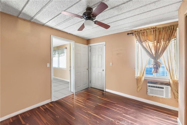 unfurnished bedroom with an AC wall unit, a ceiling fan, baseboards, and wood finished floors
