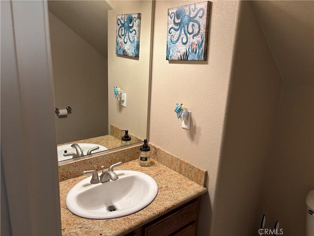 bathroom featuring a textured wall, toilet, and vanity