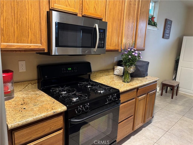 kitchen featuring stainless steel microwave, black gas range, light tile patterned floors, and brown cabinets