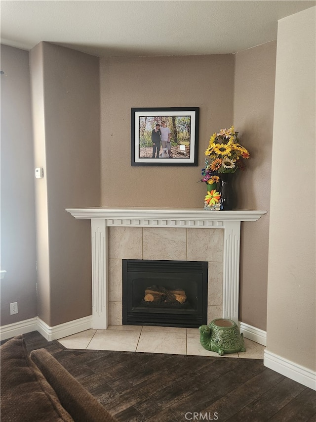details featuring a tiled fireplace, baseboards, and wood finished floors