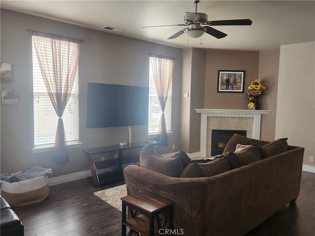 living area featuring dark wood-style flooring, visible vents, baseboards, ceiling fan, and a tiled fireplace
