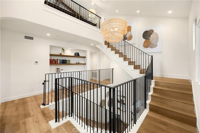 stairway with wood finished floors, visible vents, baseboards, a high ceiling, and recessed lighting