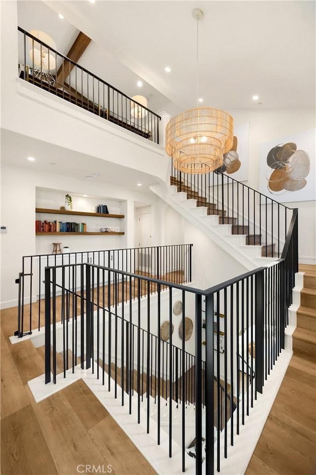 stairway featuring wood finished floors, baseboards, an inviting chandelier, a high ceiling, and recessed lighting