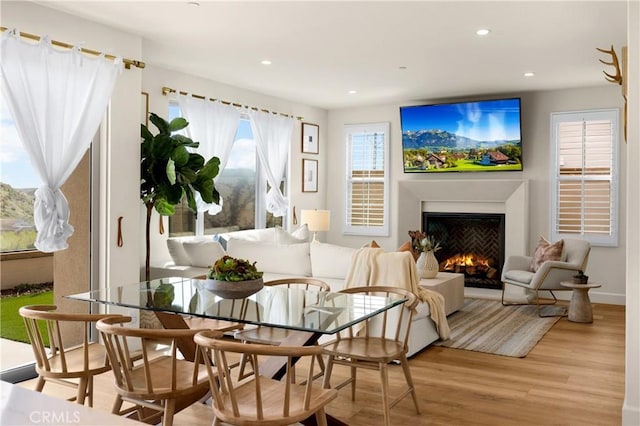 interior space with recessed lighting, a warm lit fireplace, baseboards, and light wood-style floors