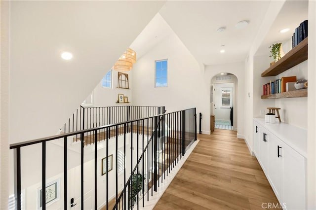 hall with arched walkways, recessed lighting, light wood-style flooring, and a wealth of natural light