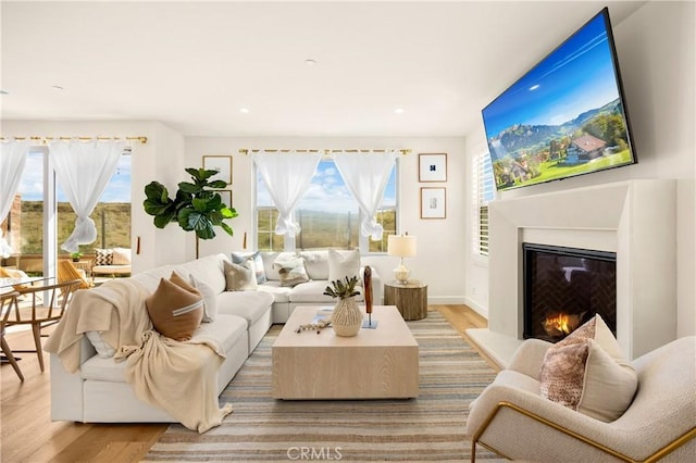 living room with recessed lighting, a warm lit fireplace, baseboards, and wood finished floors