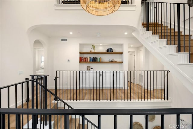 staircase with wood finished floors, visible vents, a high ceiling, recessed lighting, and arched walkways