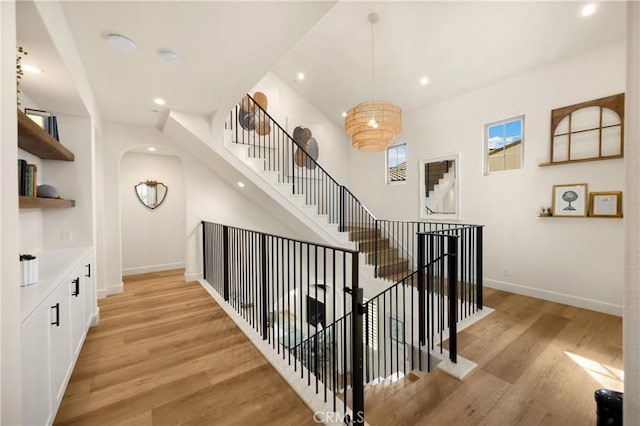 stairway with wood finished floors, recessed lighting, arched walkways, baseboards, and a chandelier