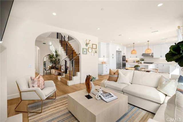 living room featuring recessed lighting, arched walkways, light wood finished floors, baseboards, and stairs