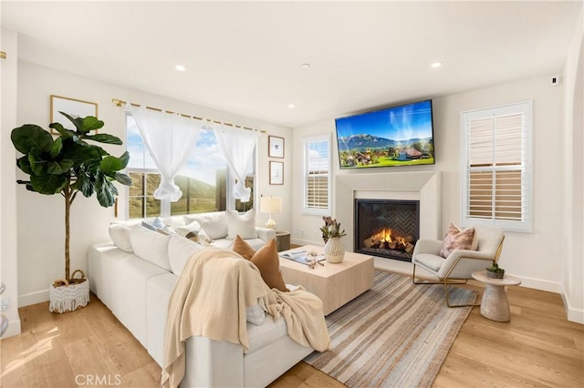 living area with recessed lighting, light wood-type flooring, and a warm lit fireplace