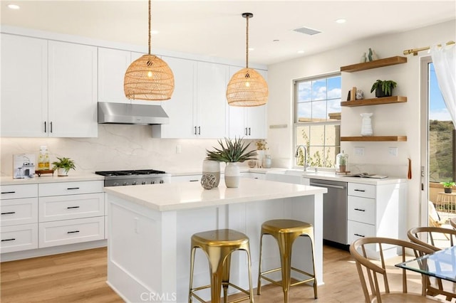 kitchen featuring under cabinet range hood, open shelves, a sink, a kitchen island, and dishwasher