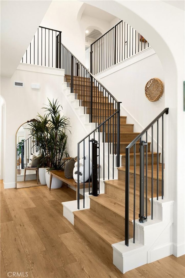 staircase with visible vents, wood finished floors, arched walkways, and baseboards