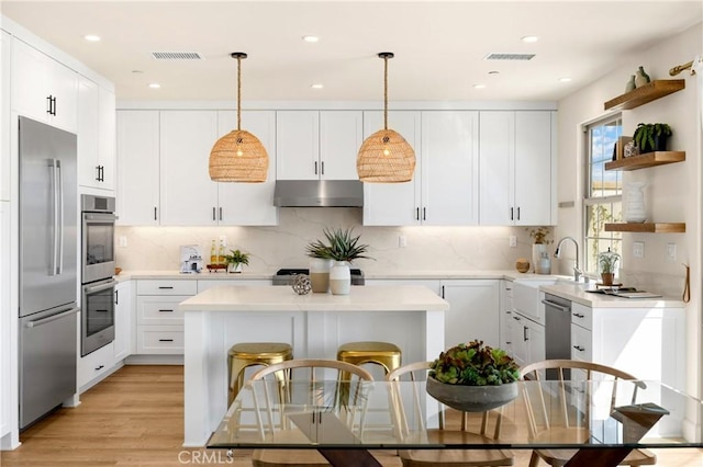 kitchen with under cabinet range hood, stainless steel appliances, a kitchen island, and visible vents