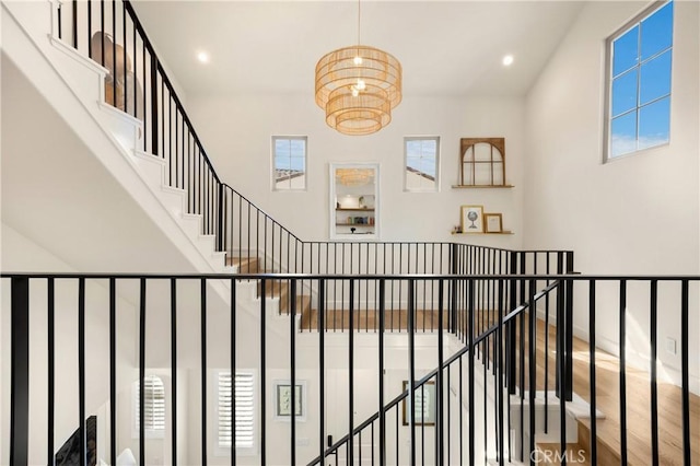 stairway with recessed lighting, an inviting chandelier, wood finished floors, and a towering ceiling