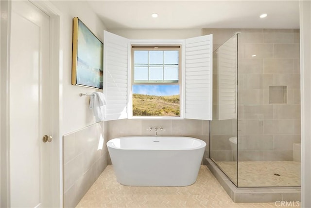 full bath featuring a shower stall, a soaking tub, recessed lighting, and tile walls