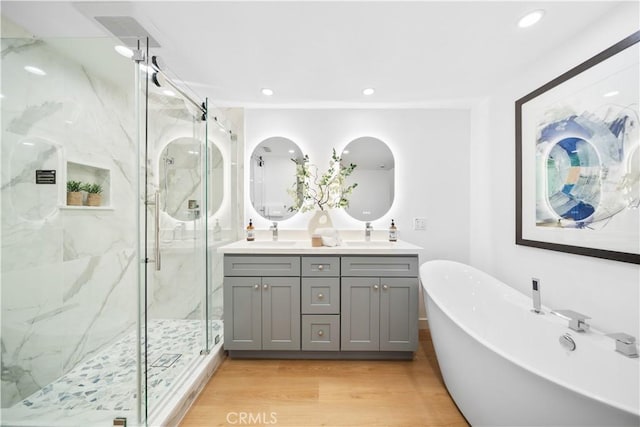 bathroom with a marble finish shower, a freestanding bath, double vanity, wood finished floors, and a sink