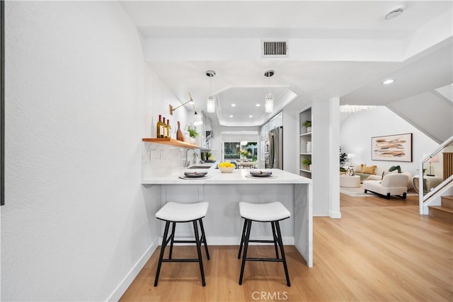 kitchen with open shelves, a breakfast bar, stainless steel refrigerator, and light wood finished floors