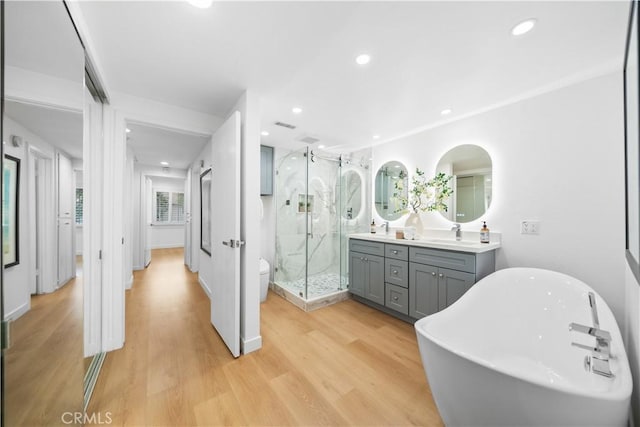 full bath featuring a shower stall, wood finished floors, recessed lighting, a freestanding tub, and vanity