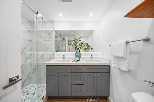full bath featuring a sink, a marble finish shower, toilet, and double vanity