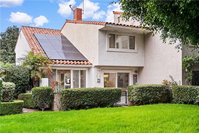 rear view of property featuring stucco siding, roof mounted solar panels, a yard, a chimney, and a tiled roof