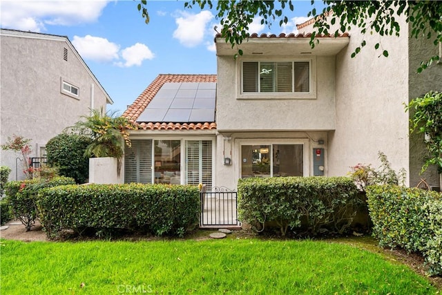 view of front of property featuring stucco siding, roof mounted solar panels, a front lawn, and a tile roof