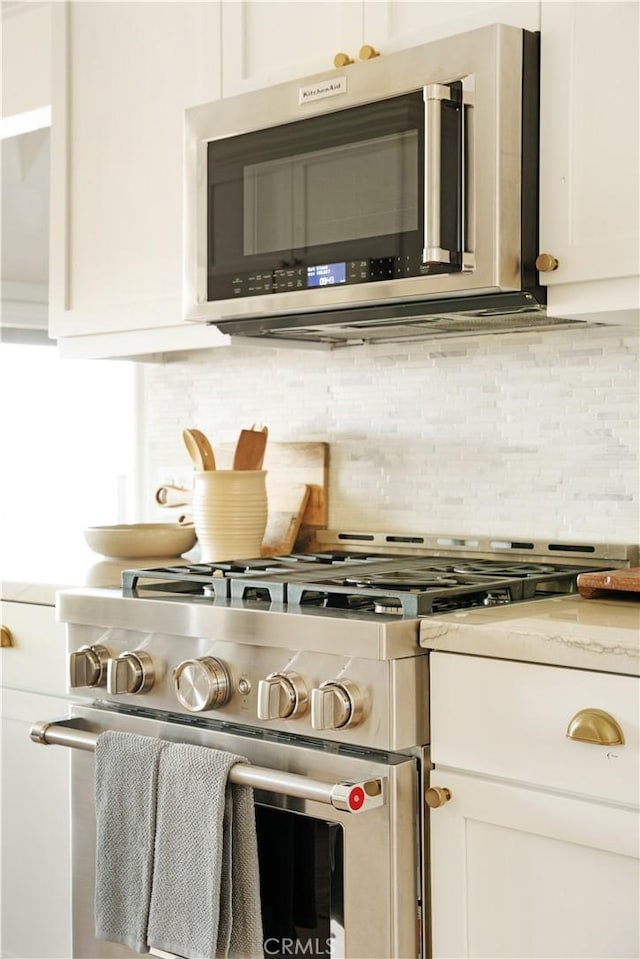 kitchen with stainless steel appliances, tasteful backsplash, light stone countertops, and white cabinets