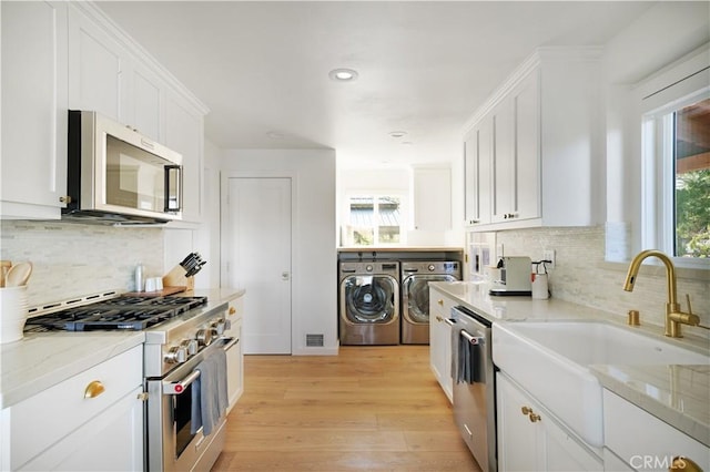 kitchen featuring white cabinetry, appliances with stainless steel finishes, a sink, light wood finished floors, and washer and clothes dryer