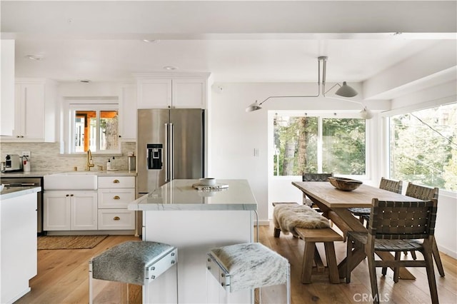 kitchen with tasteful backsplash, a sink, light wood-style floors, high end fridge, and white cabinetry