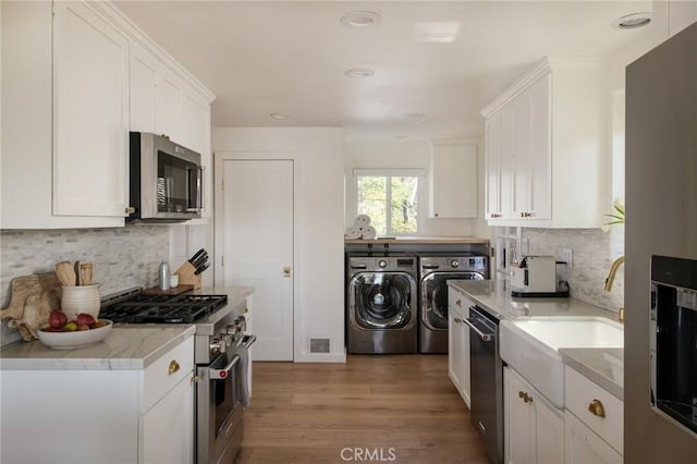 kitchen featuring visible vents, light wood-type flooring, white cabinetry, stainless steel appliances, and washing machine and dryer