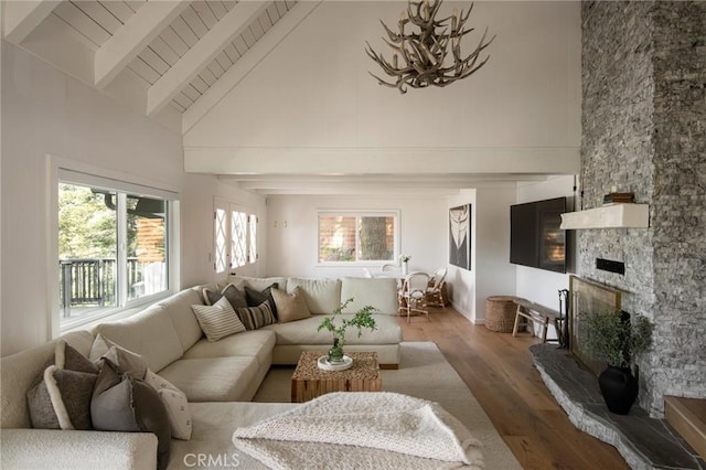 living area with a stone fireplace, a chandelier, beamed ceiling, wood ceiling, and wood finished floors