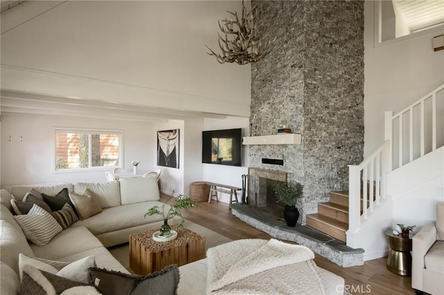 living room featuring wood finished floors, a high ceiling, a stone fireplace, and stairs