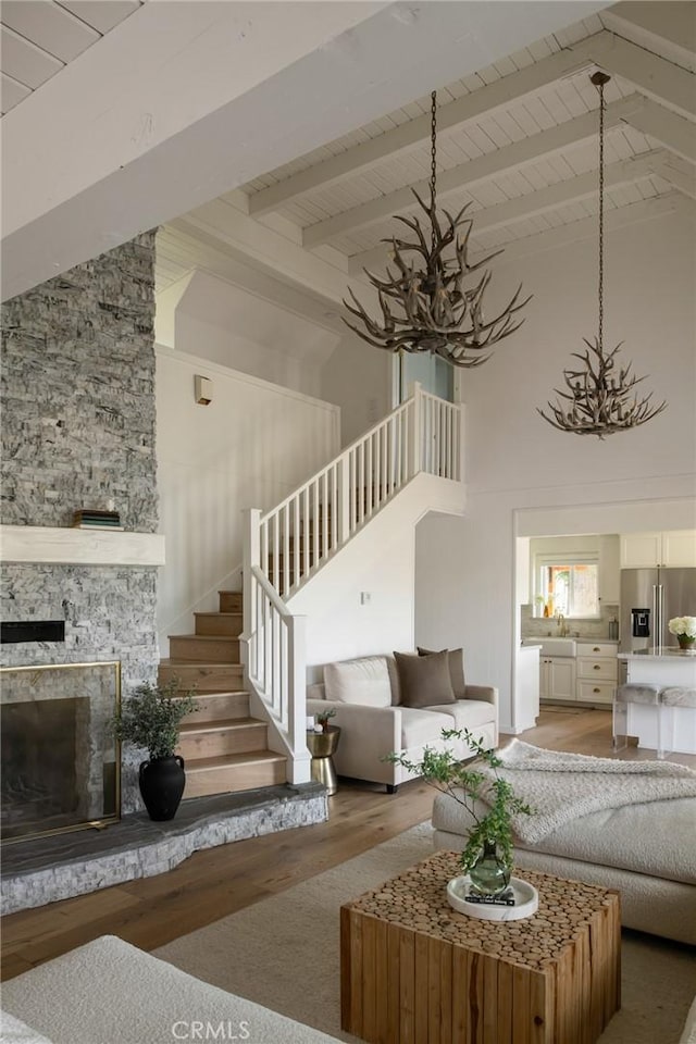 unfurnished living room featuring an inviting chandelier, a fireplace, light wood-style flooring, stairway, and beam ceiling