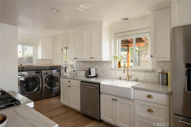 kitchen featuring separate washer and dryer, a sink, light wood-style floors, white cabinetry, and stainless steel appliances