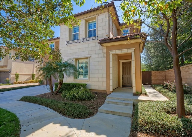 mediterranean / spanish house featuring a tile roof, fence, and concrete driveway