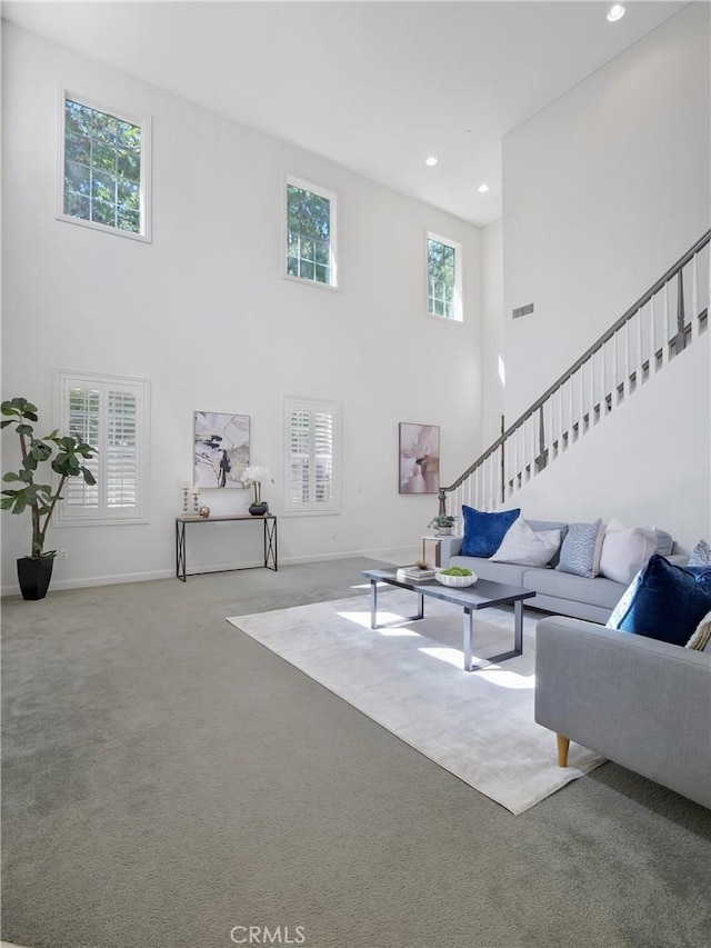 carpeted living area featuring stairs, a high ceiling, baseboards, visible vents, and recessed lighting