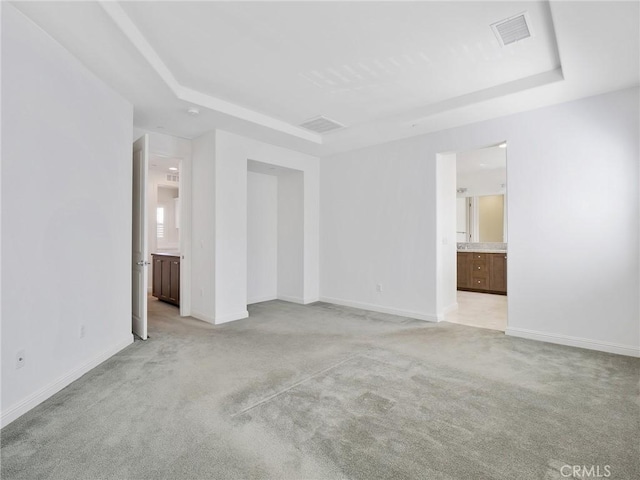 spare room featuring light carpet, baseboards, visible vents, and a raised ceiling