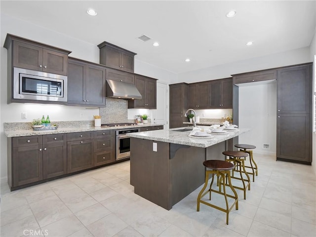 kitchen with stainless steel appliances, range hood, a sink, visible vents, and dark brown cabinetry