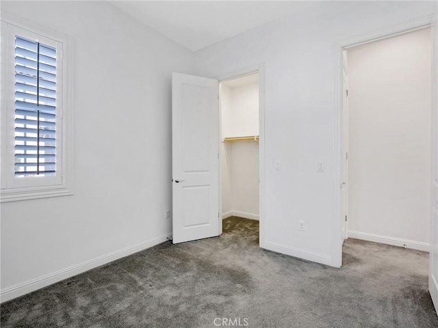 unfurnished bedroom with baseboards, carpet floors, and a walk in closet