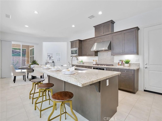 kitchen featuring visible vents, appliances with stainless steel finishes, a sink, extractor fan, and a breakfast bar area