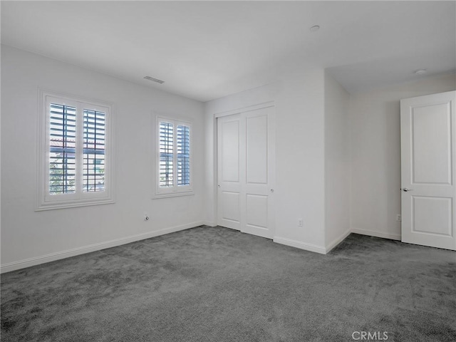 spare room with baseboards, visible vents, and dark colored carpet