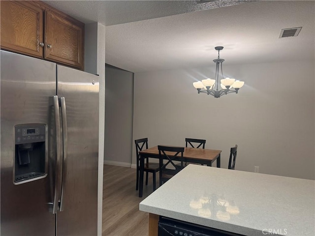 kitchen featuring visible vents, light wood finished floors, light countertops, stainless steel refrigerator with ice dispenser, and a notable chandelier