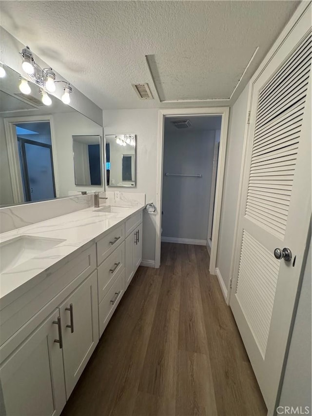 full bathroom featuring visible vents, a sink, a textured ceiling, wood finished floors, and double vanity