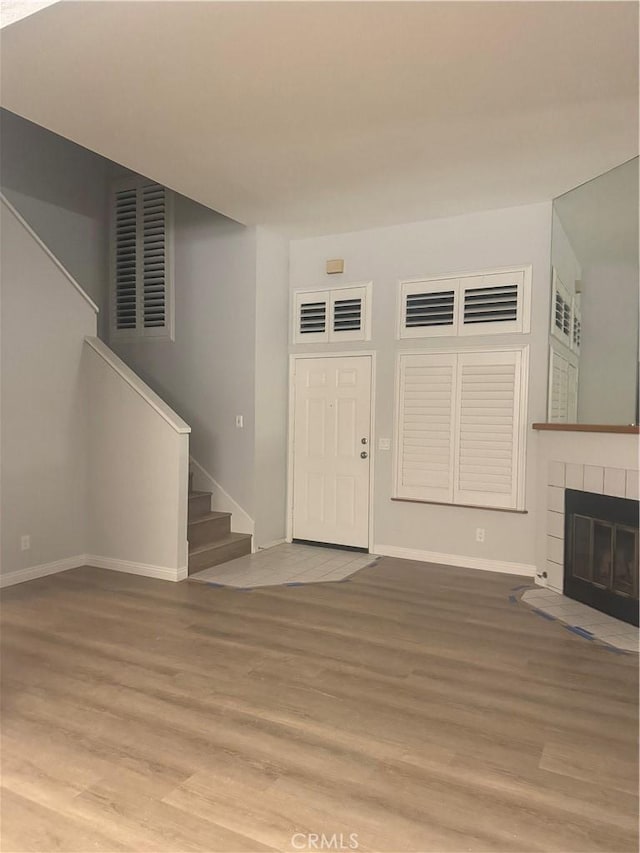 unfurnished living room with wood finished floors, baseboards, visible vents, a fireplace, and stairs